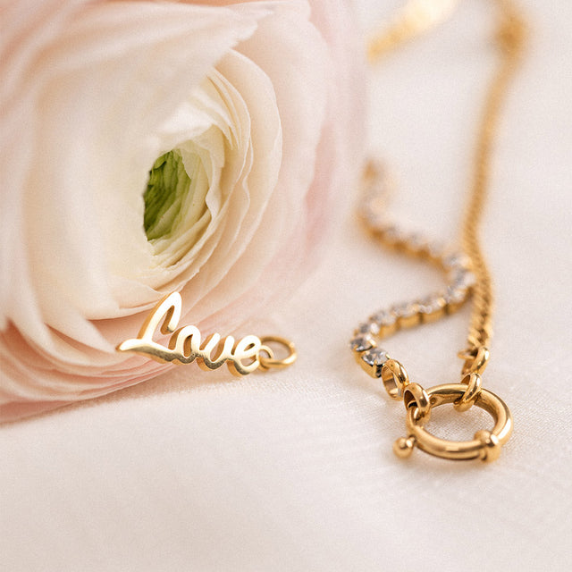 Love Charm Anhänger aus 18K Gold Edelstahl, elegant auf hellem Stoff mit zarter Blüte, PURELEI Signature.