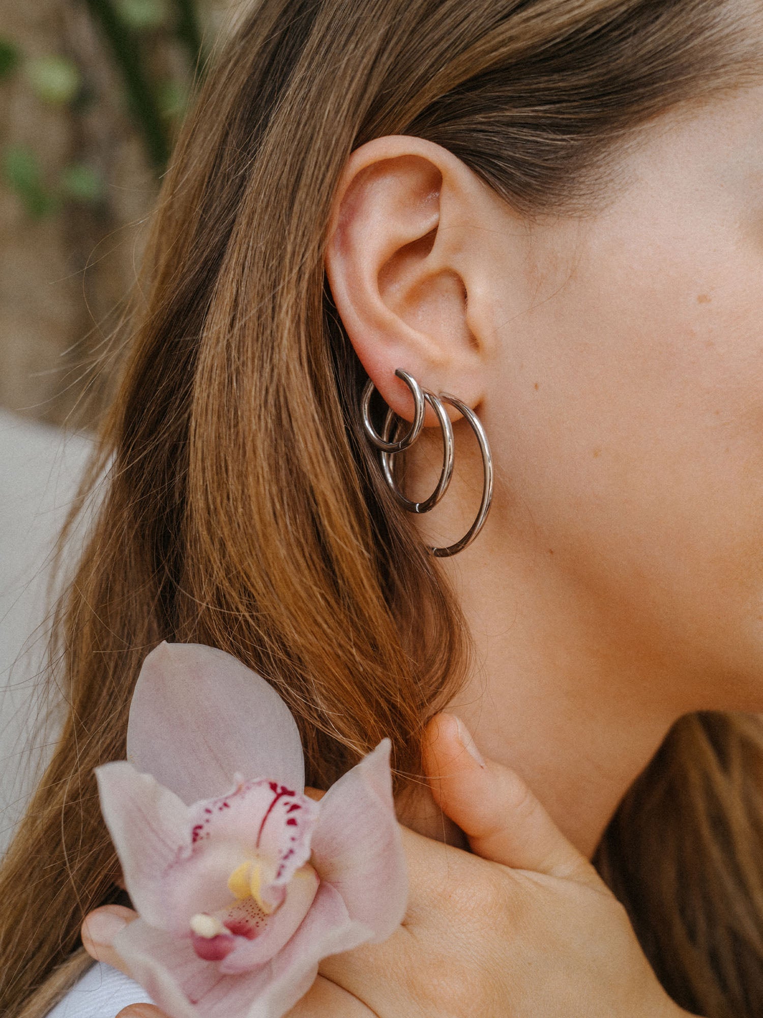 Nickelfreie, silberne Creolen von PURELEI, elegant und modern, getragen mit einer Blüte.