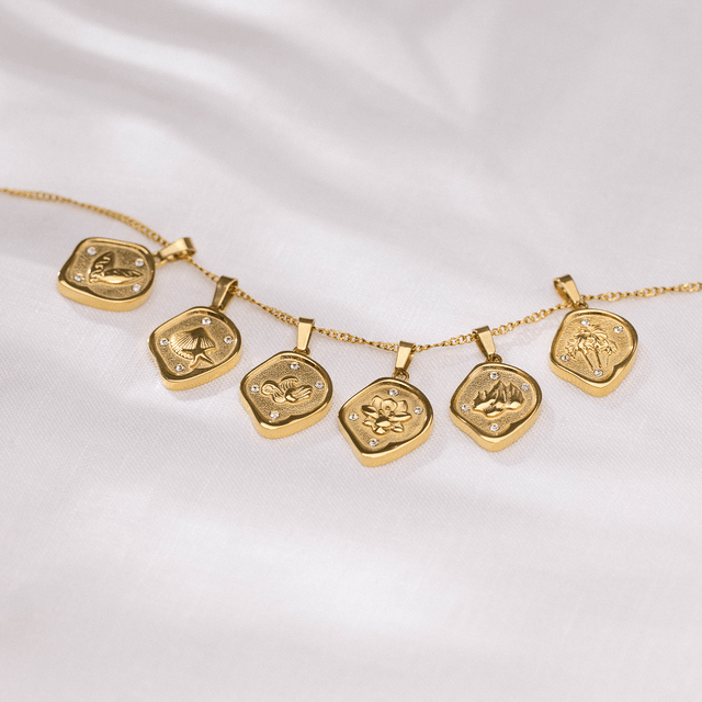 Surfboards Coin Charm von PURELEI, goldene Anhänger mit Surfboard-Motiven und funkelnden Zirkonia auf weißem Stoff