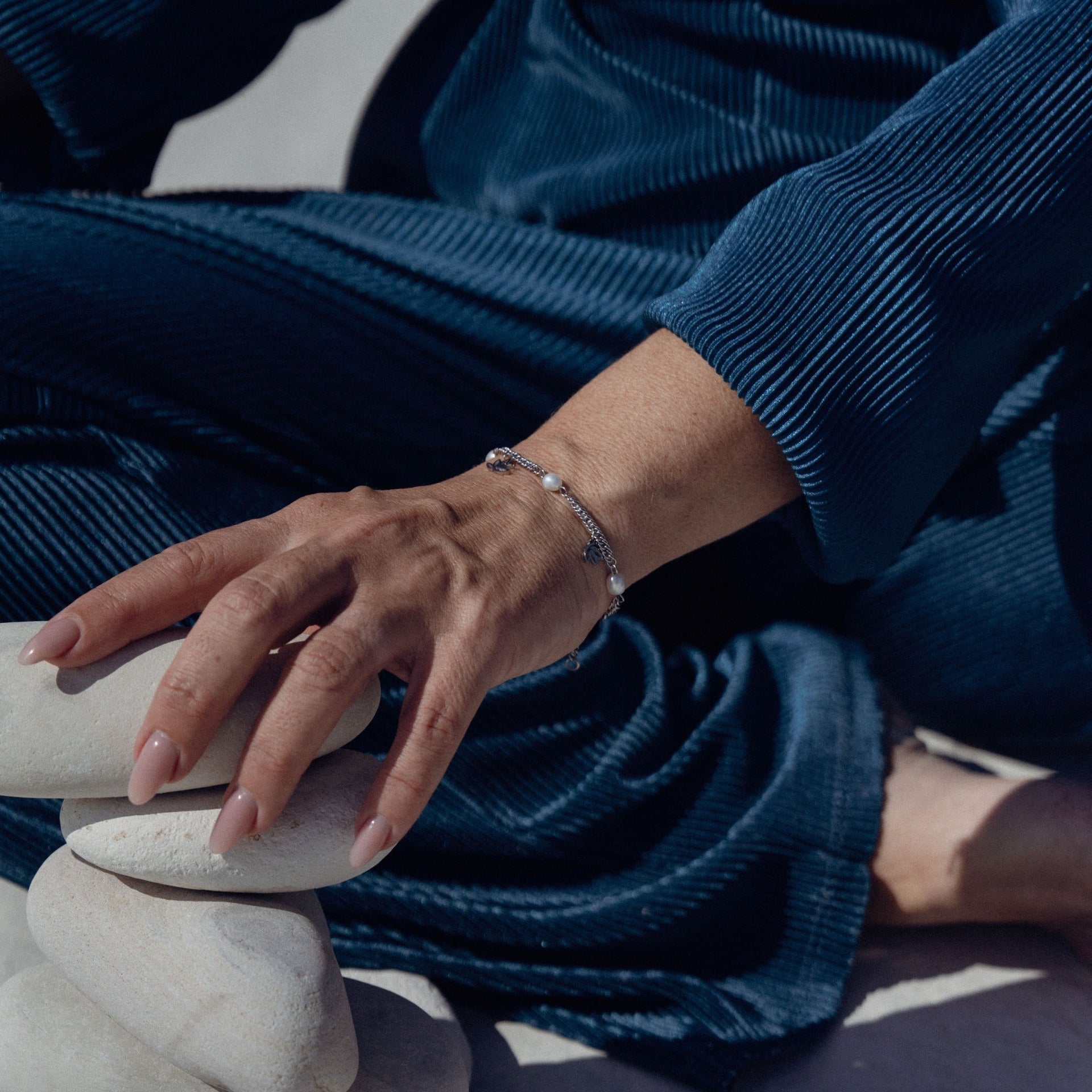 Silbernes Armband mit Perlen, getragen auf einer Hand, umgeben von weißen Steinen – PURELEI.
