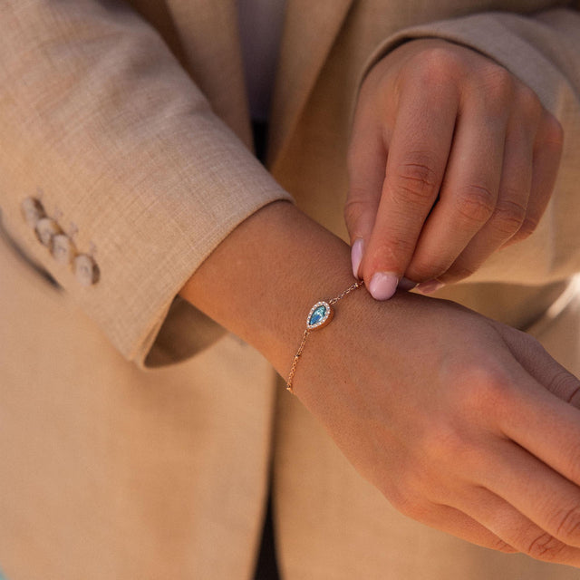 PURELEI Bellezza Armband in vergoldetem Edelstahl mit blauem Tropfenstein und weißen Akzenten am Handgelenk.