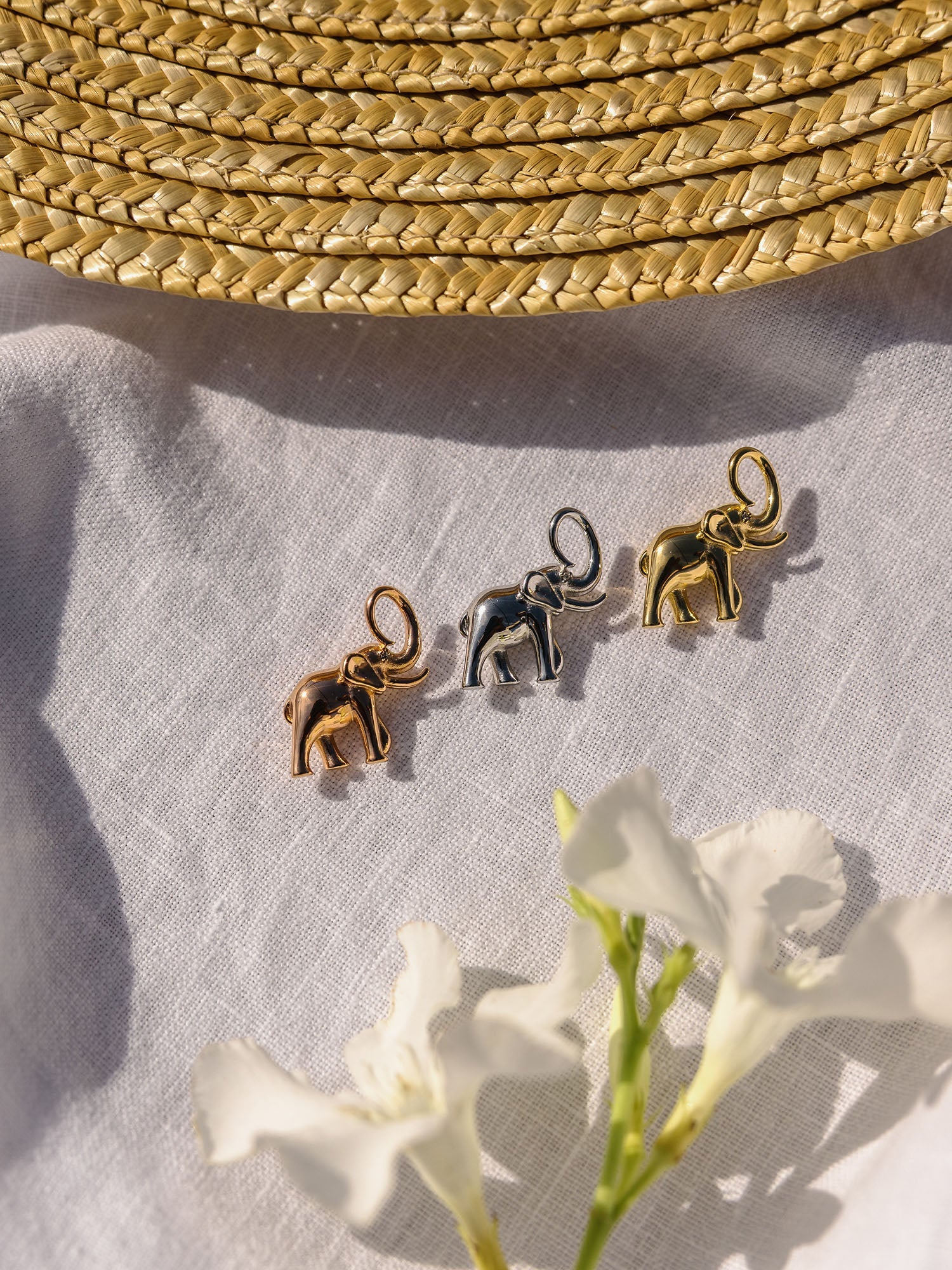 Drei PURELEI Flowing Strength Elefant Charms in Gold, Silber und Roségold auf Leinen in warmem Sonnenlicht.