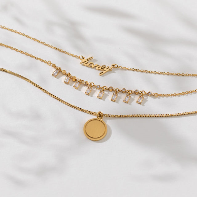 PURELEI Honey Kette aus 18K Gold Edelstahl mit geschwungenem Schriftzug, elegant und feminin auf weißem Leinen.