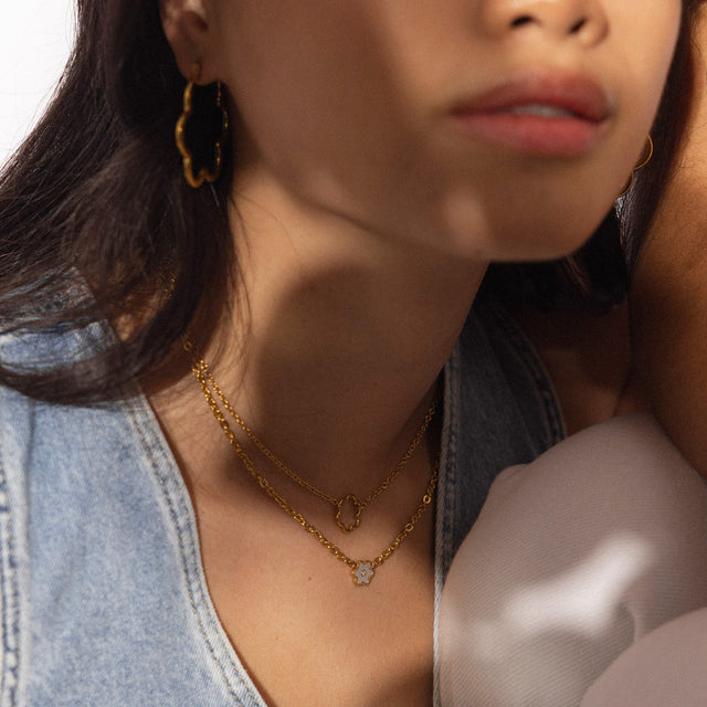 PURELEI Bloom Kette aus goldfarbenem Edelstahl mit filigranem Blütenanhänger, elegant geschichtet getragen.