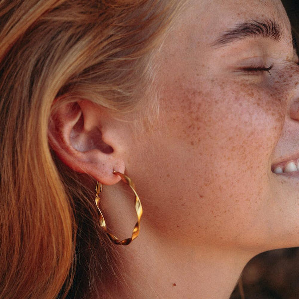 PURELEI Ke Kai Ohrringe aus 18K Gold mit leicht verdrehter Creolenform, warm und elegant am Ohr getragen.