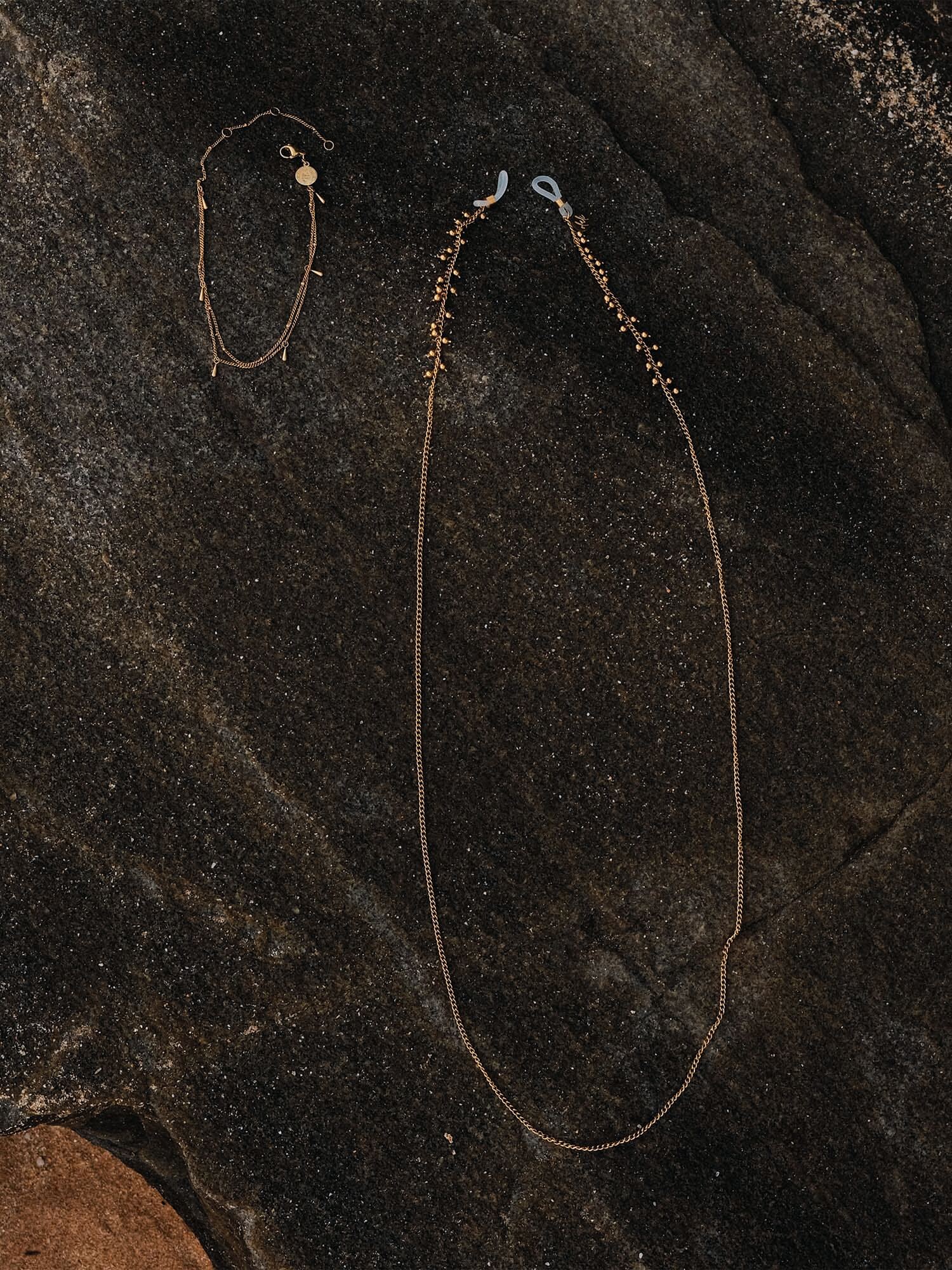 Zarte goldene Kette und Armband von PURELEI auf dunklem Stein, elegant und modern.