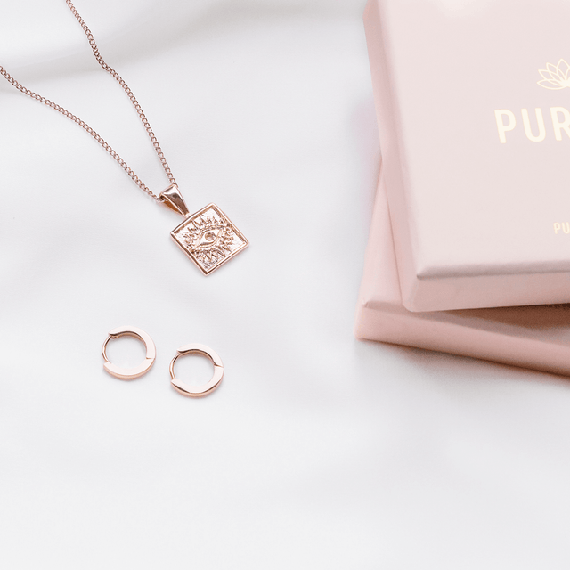 PURELEI Ike Ohrringe aus roségoldenem Edelstahl als feine Creolen, elegant auf weißem Stoff inszeniert.