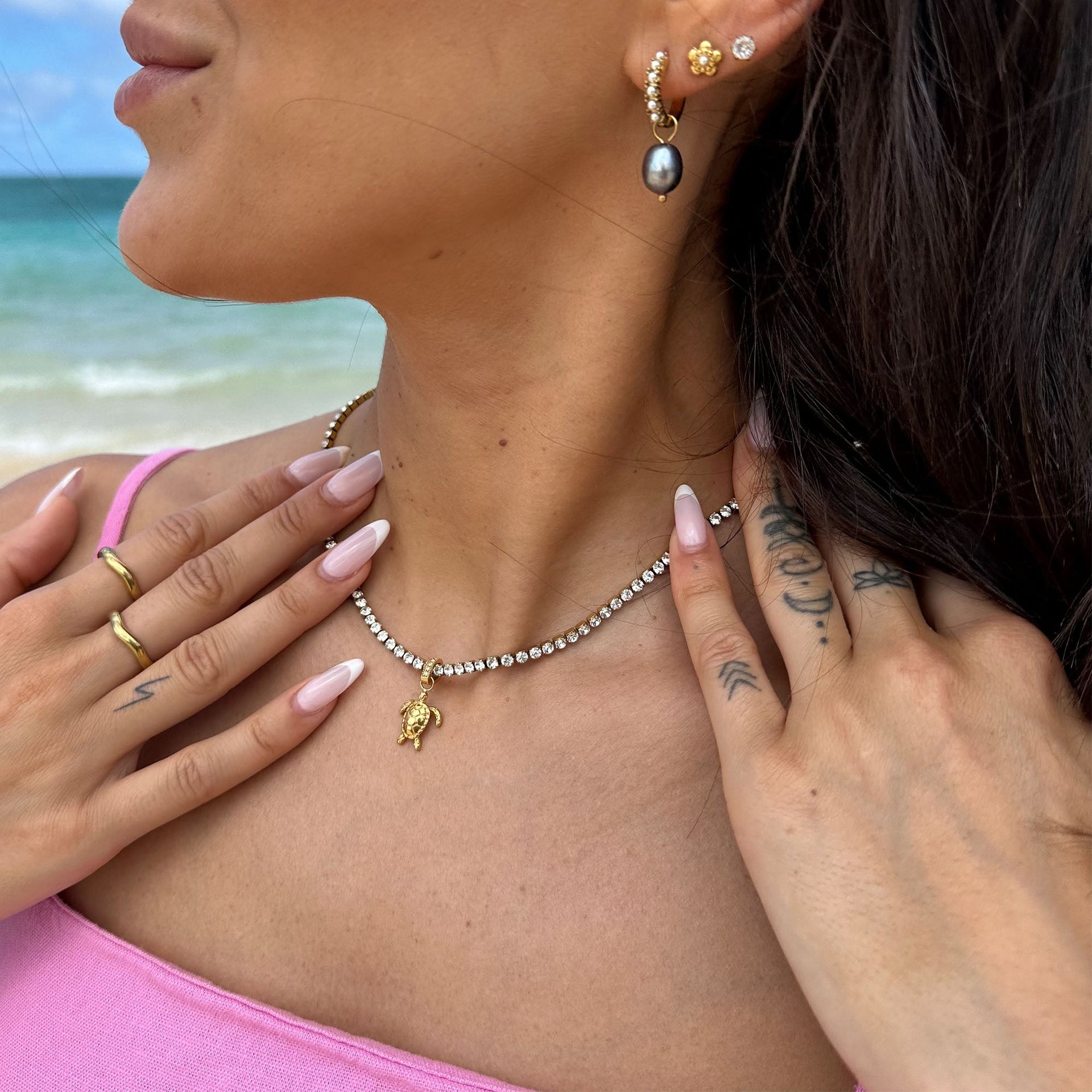 Glitzernde PURELEI Kette mit Muschel-Anhänger, getragen am Hals, umgeben von tropischem Flair.