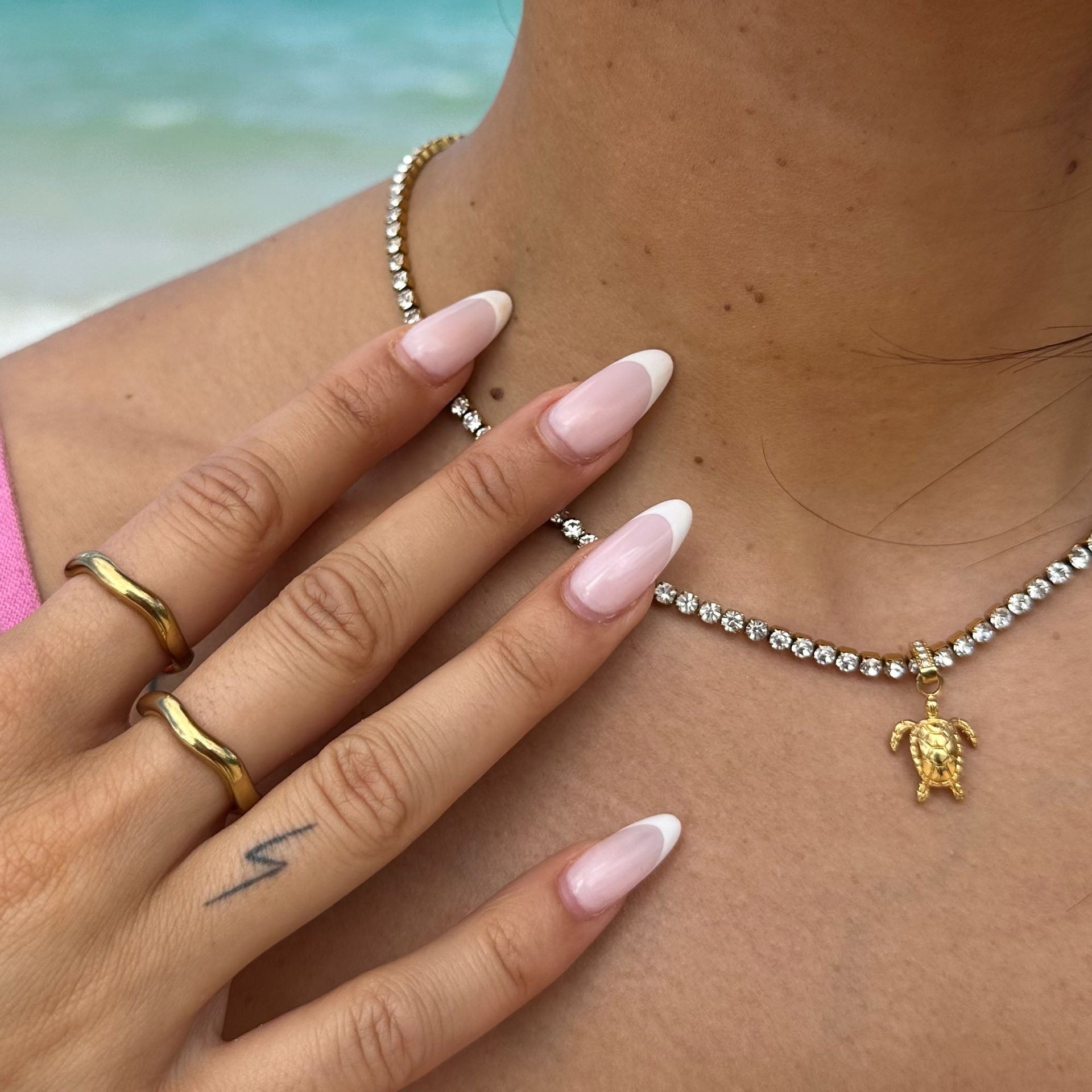 Glitzernde PURELEI Halskette mit Schildkröten-Anhänger, getragen mit eleganten Ringen.