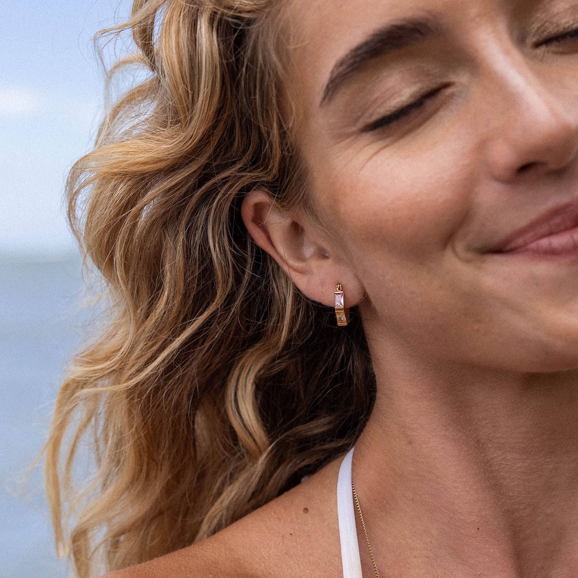 Roségoldene Creolen mit elegantem Design, getragen von einer lächelnden Frau am Strand – PURELEI.
