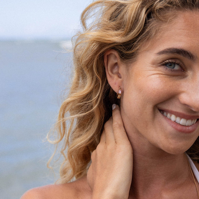 Roségoldene Creolen von PURELEI, elegant und strahlend, am Ohr einer lächelnden Frau.