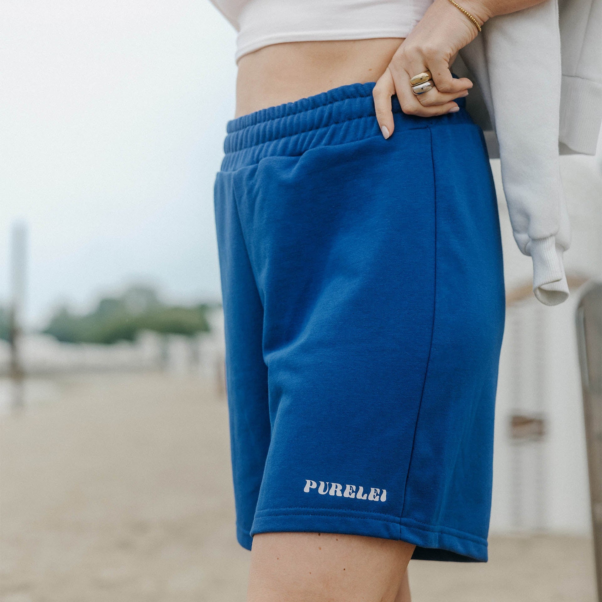 Blue Paradise Shorts aus dunkelblauer Baumwolle mit PURELEI-Logo, sommerlich und bequem getragen am Strand.