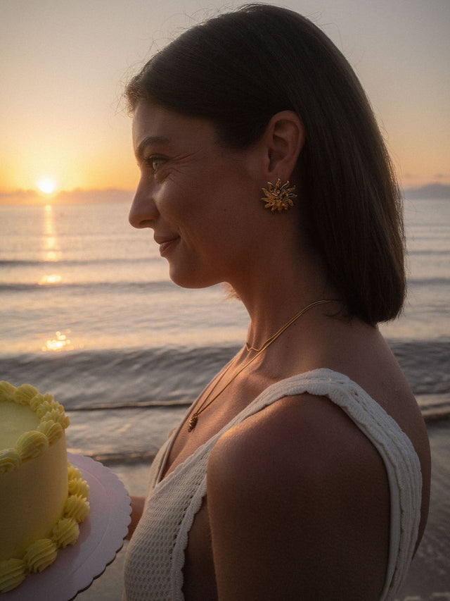 PURELEI Iconic Sun Ohrringe aus goldfarbenem Edelstahl mit Sonnenmotiv am Strand bei Sonnenuntergang