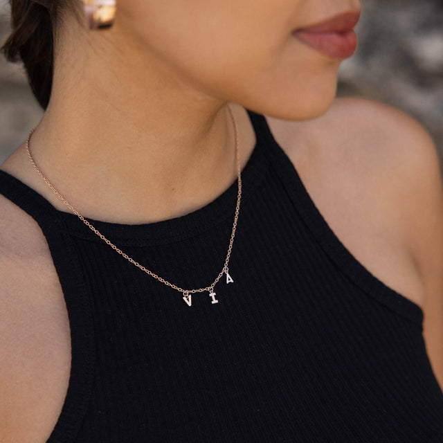 Goldene PURELEI Kette mit Buchstabenanhängern, getragen auf schwarzem Oberteil.