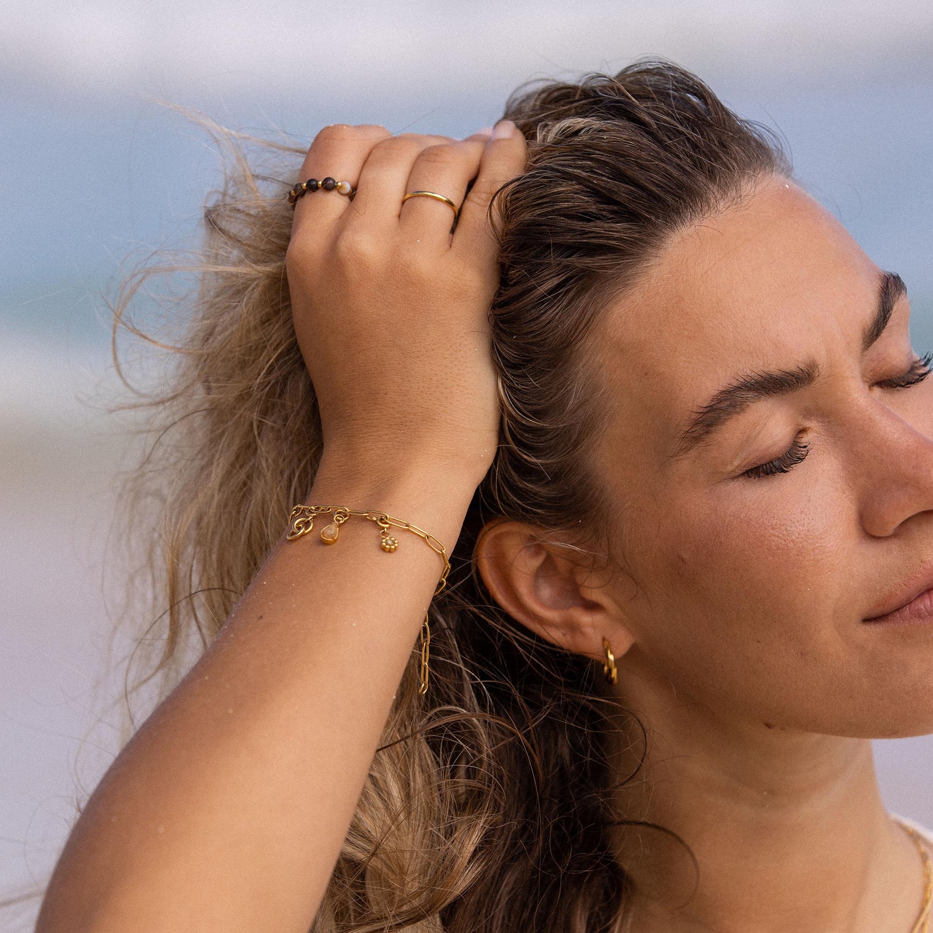 PURELEI Anxiety Mahina Club Mokupuni Ring aus vergoldetem Edelstahl mit Natursteinperlen am Strand getragen.