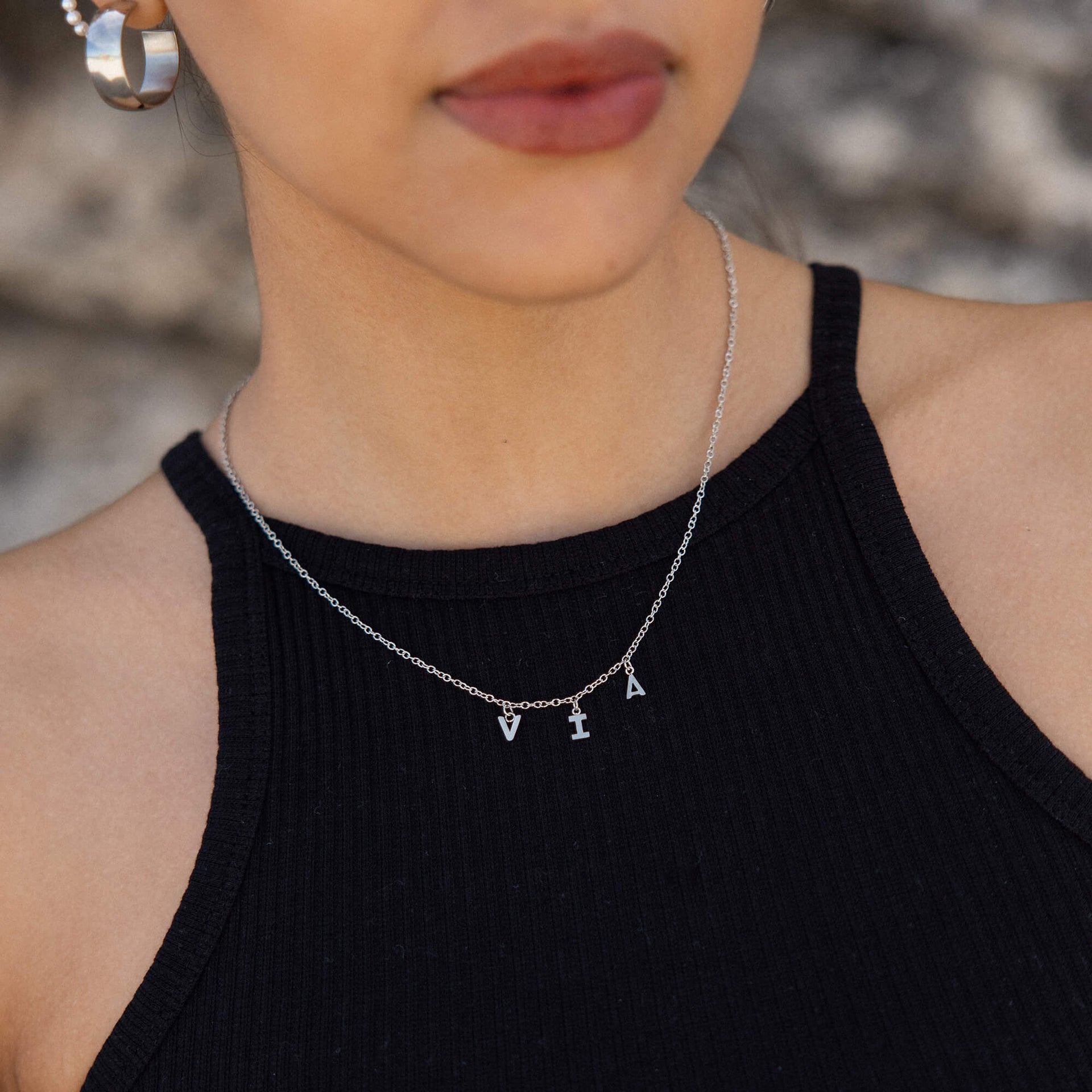 Silberne Buchstaben-Halskette von PURELEI, elegant und modern, getragen auf schwarzem Top.