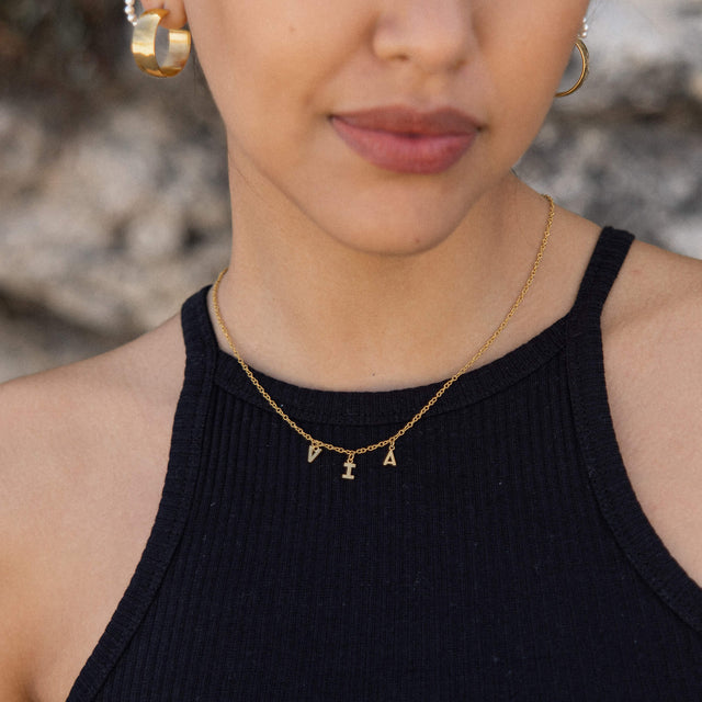 Roségoldene Kette mit Buchstabenanhängern, getragen mit schwarzem Oberteil – PURELEI.