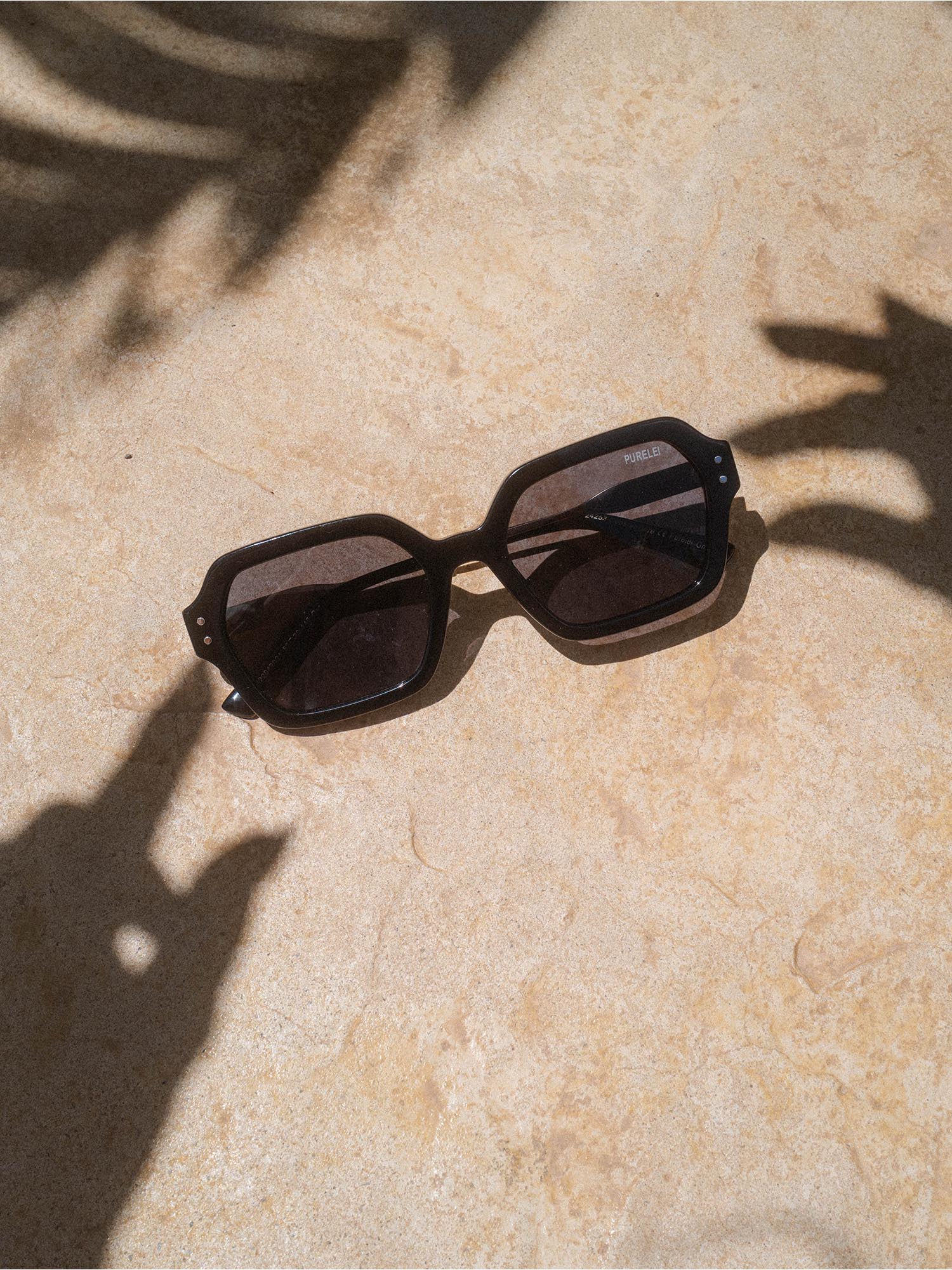 Coastal Core Sonnenbrille von PURELEI, schwarzer Acetat-Rahmen, markantes oval-eckiges Design, elegant in Sonnenlicht.