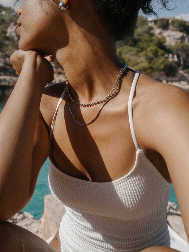 Silberne PURELEI Kette und Ohrringe, getragen in sonniger, entspannter Atmosphäre am Wasser.