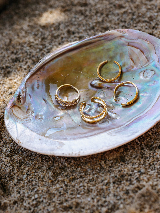 Silberne Ringe auf einer Muschel, inspiriert von PURELEI, am Sand platziert.