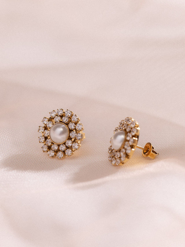 Roségoldene Ohrringe mit Perle und funkelnden Steinen von PURELEI auf sanftem Stoff.