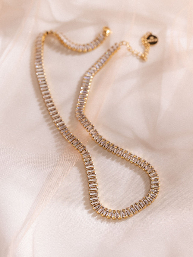 Elegante goldene Kette mit funkelnden Details auf zartem Stoff, PURELEI.