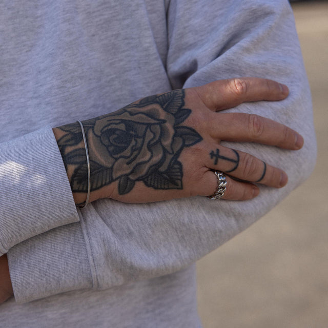 Silbernes Armband und Ring von PURELEI, getragen mit tätowierter Hand, lässige Stimmung.