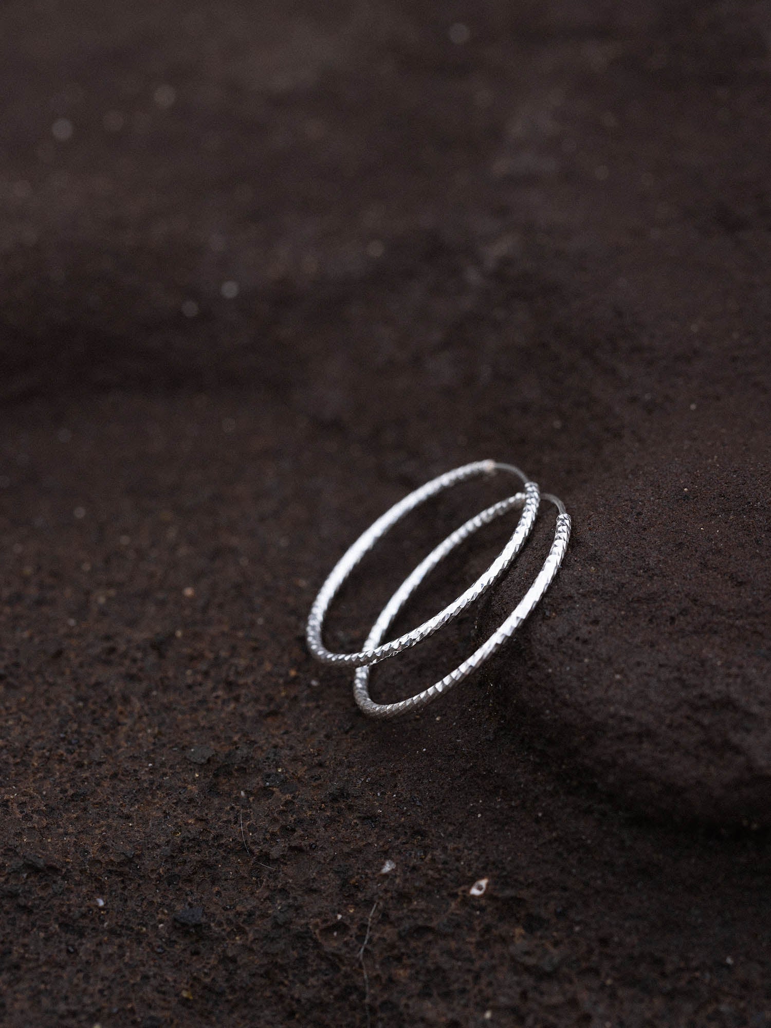 Gleam Ohrringe aus facettiertem recyceltem Silber auf dunklem Lavagestein, elegant und zeitlos von PURELEI.