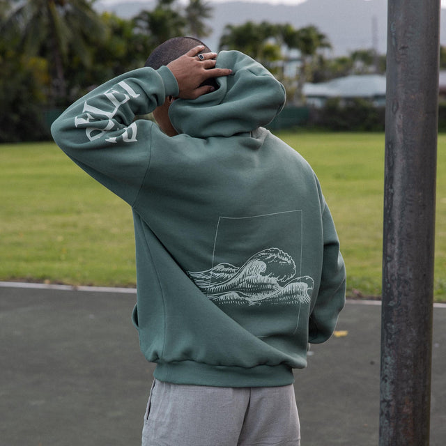 Grüne Kapuzenjacke mit Wellenmotiv, inspiriert von PURELEI, in entspannter Outdoor-Umgebung.
