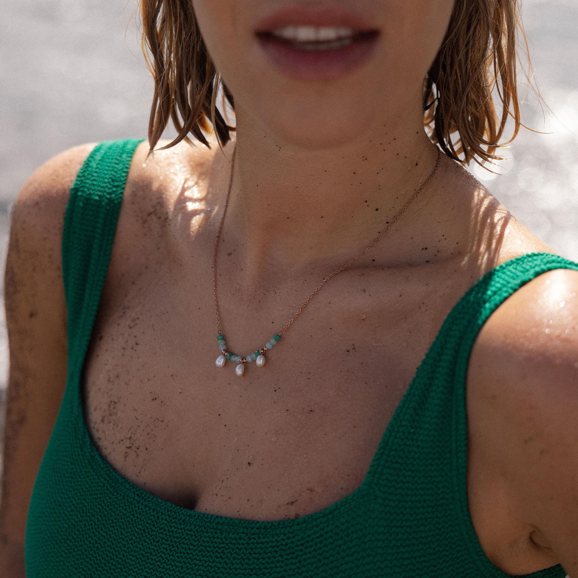 Zarte goldene Kette mit Muschel- und grünen Steinen, getragen am Strand – PURELEI.