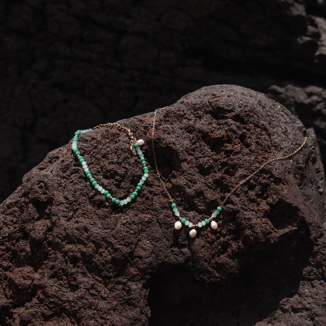 Zwei zarte Ketten mit weißen Perlen auf dunklem Lavagestein, PURELEI inspiriert.