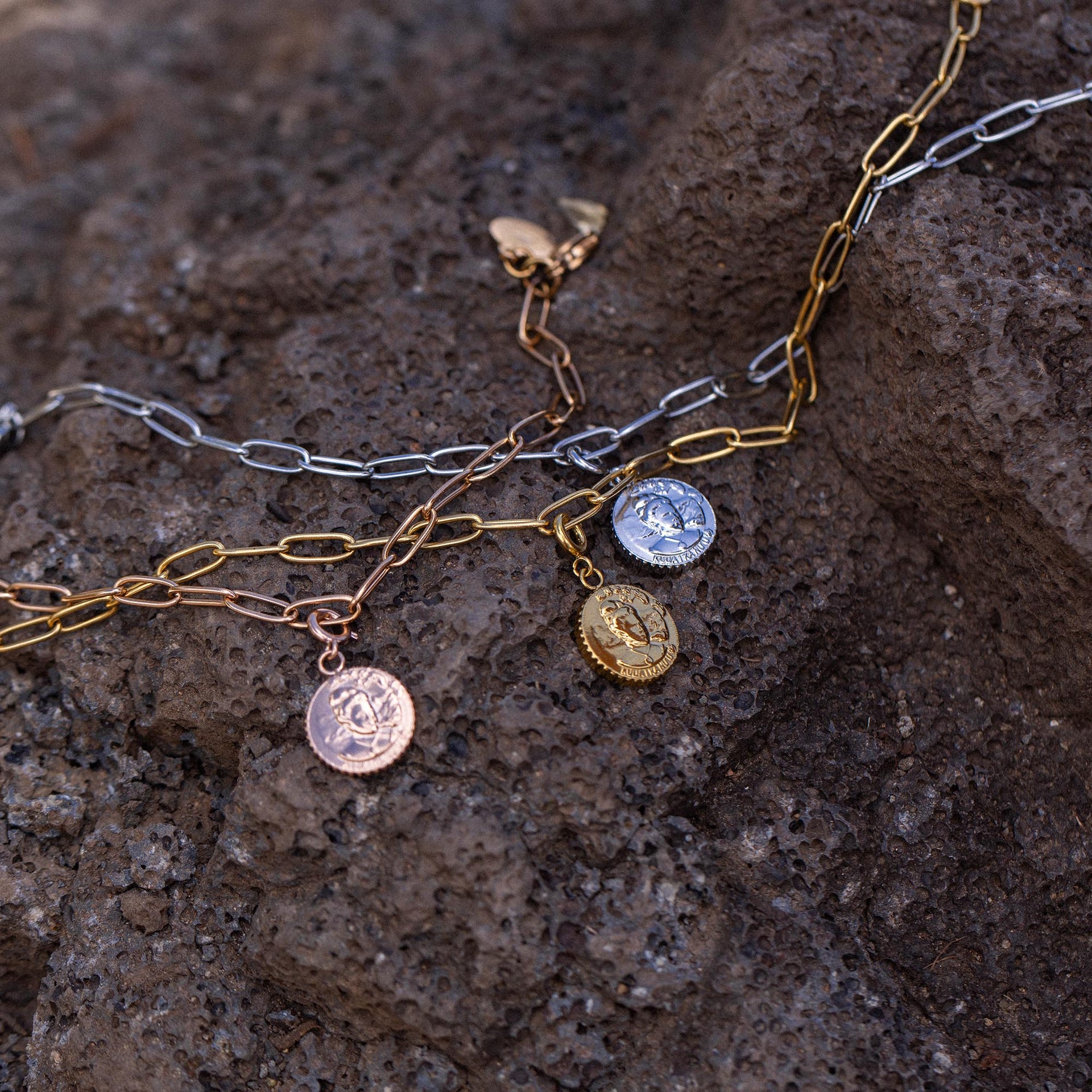 Mahina Club Lei Charm von PURELEI in Gold, Silber und Roségold auf rauem Vulkangestein, elegant und zeitlos.