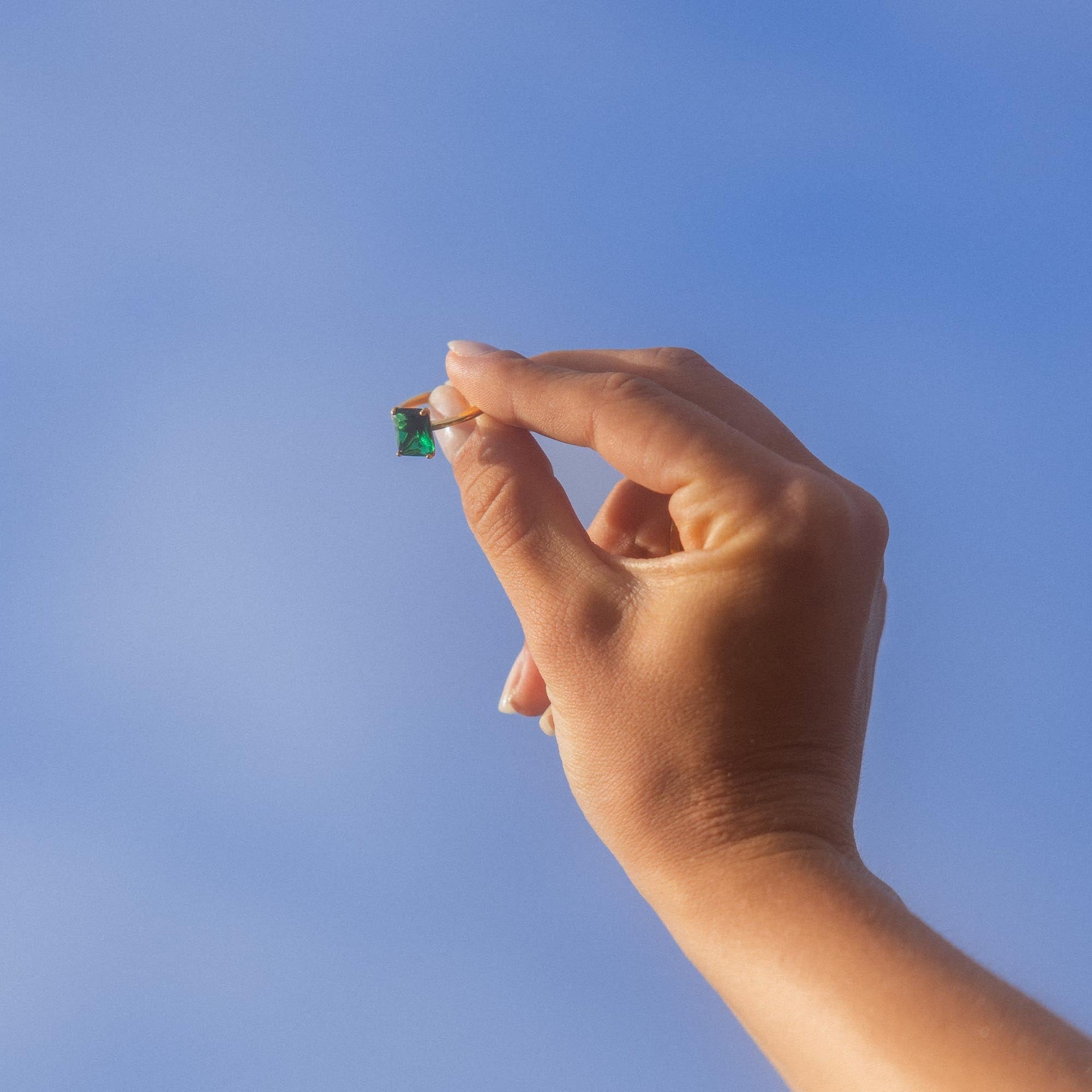 Hand hält einen kleinen, braunen Anhänger vor blauem Himmel, PURELEI inspiriert.