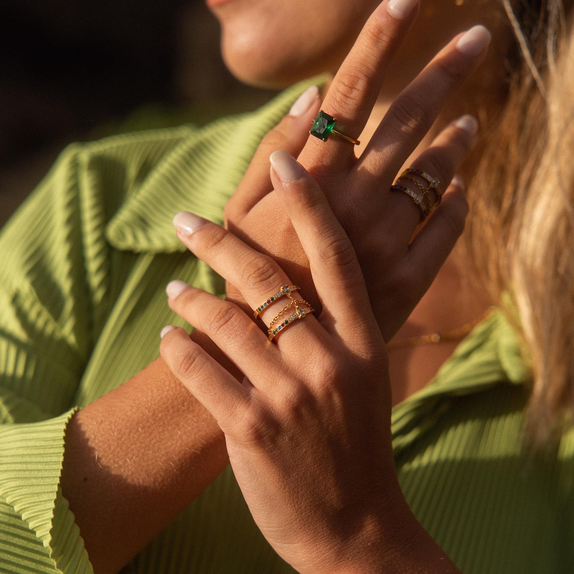 Goldene Ringe mit grünen Steinen, getragen von einer Hand, PURELEI inspiriert.