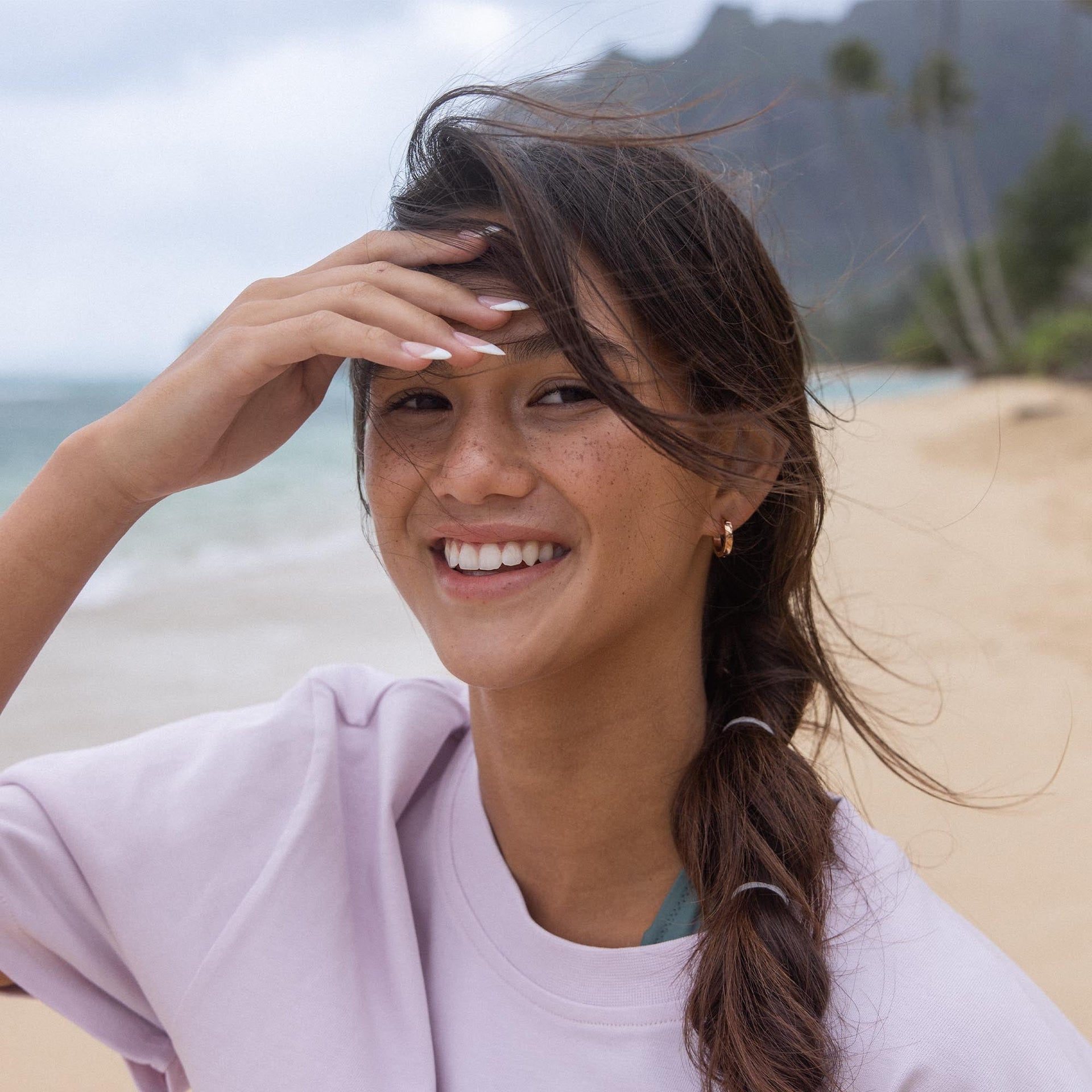 Lächelnde Frau am Strand mit PURELEI Creolen, umgeben von tropischer Leichtigkeit.
