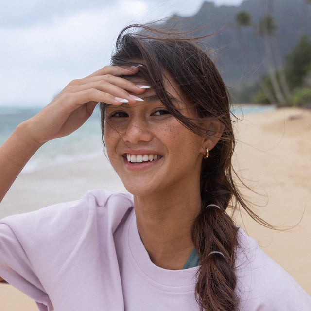 Lächelnde Frau am Strand mit PURELEI Creolen, umgeben von tropischer Leichtigkeit.