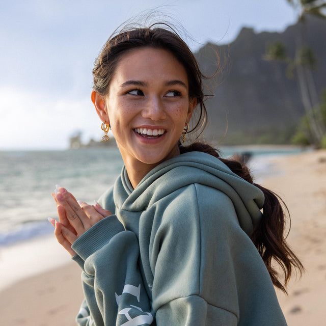 Feminine Ohrringe von PURELEI, goldfarben, am Strand getragen, strahlende Stimmung.