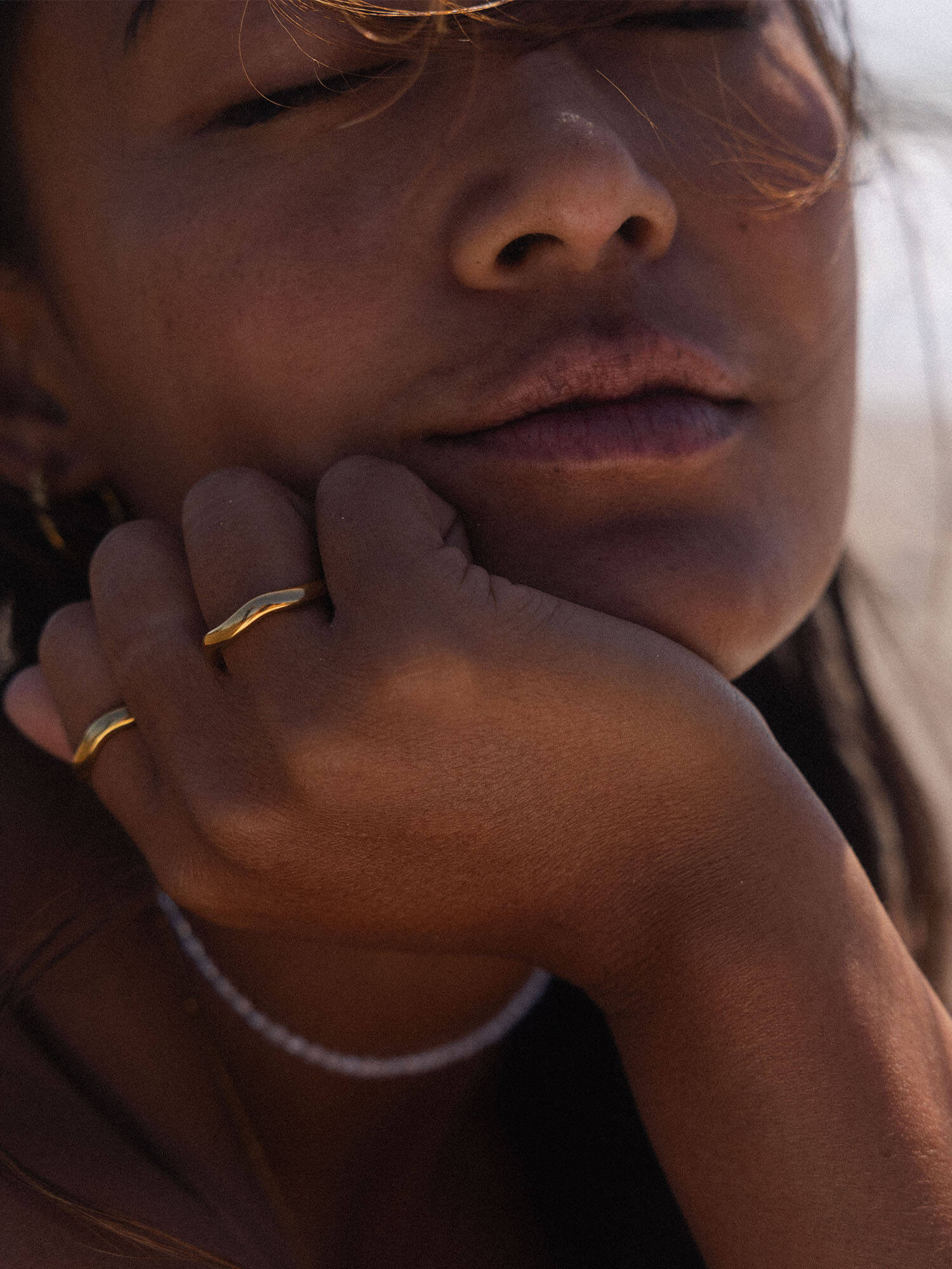 PURELEI Nakuna Ring in 18K Gold mit natürlicher Wellenform, getragen in warmem Sonnenlicht auf Haut nah am Gesicht