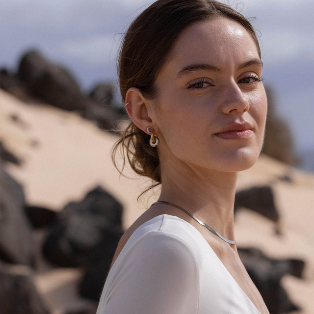 Silberne Creolen und Halskette von PURELEI, elegant und modern, vor sandigem Hintergrund.