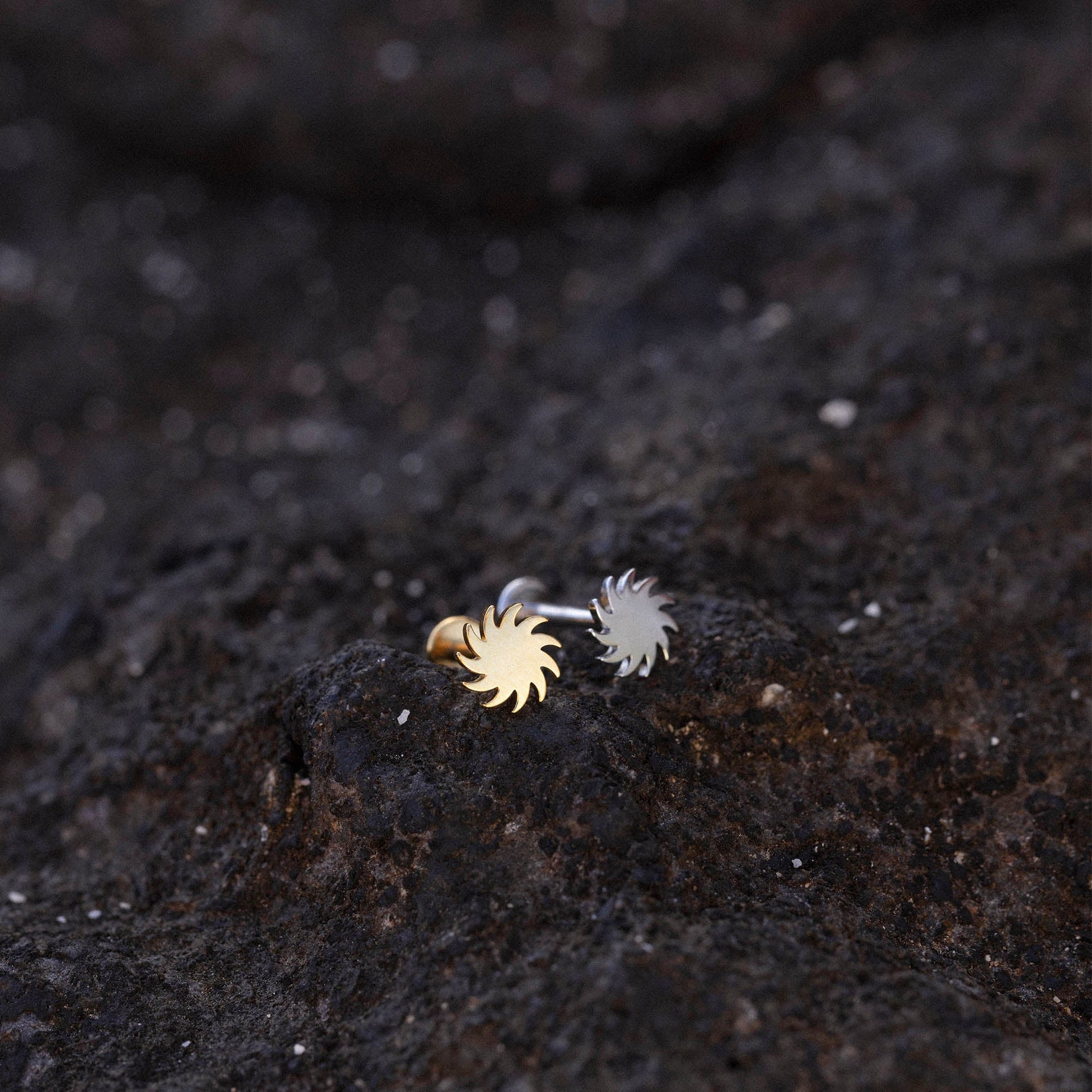 Sun Piercing von PURELEI, nickelfrei, gold- und silberfarbenes Sonnenmotiv auf dunklem Lavagestein, elegant und natürlich.
