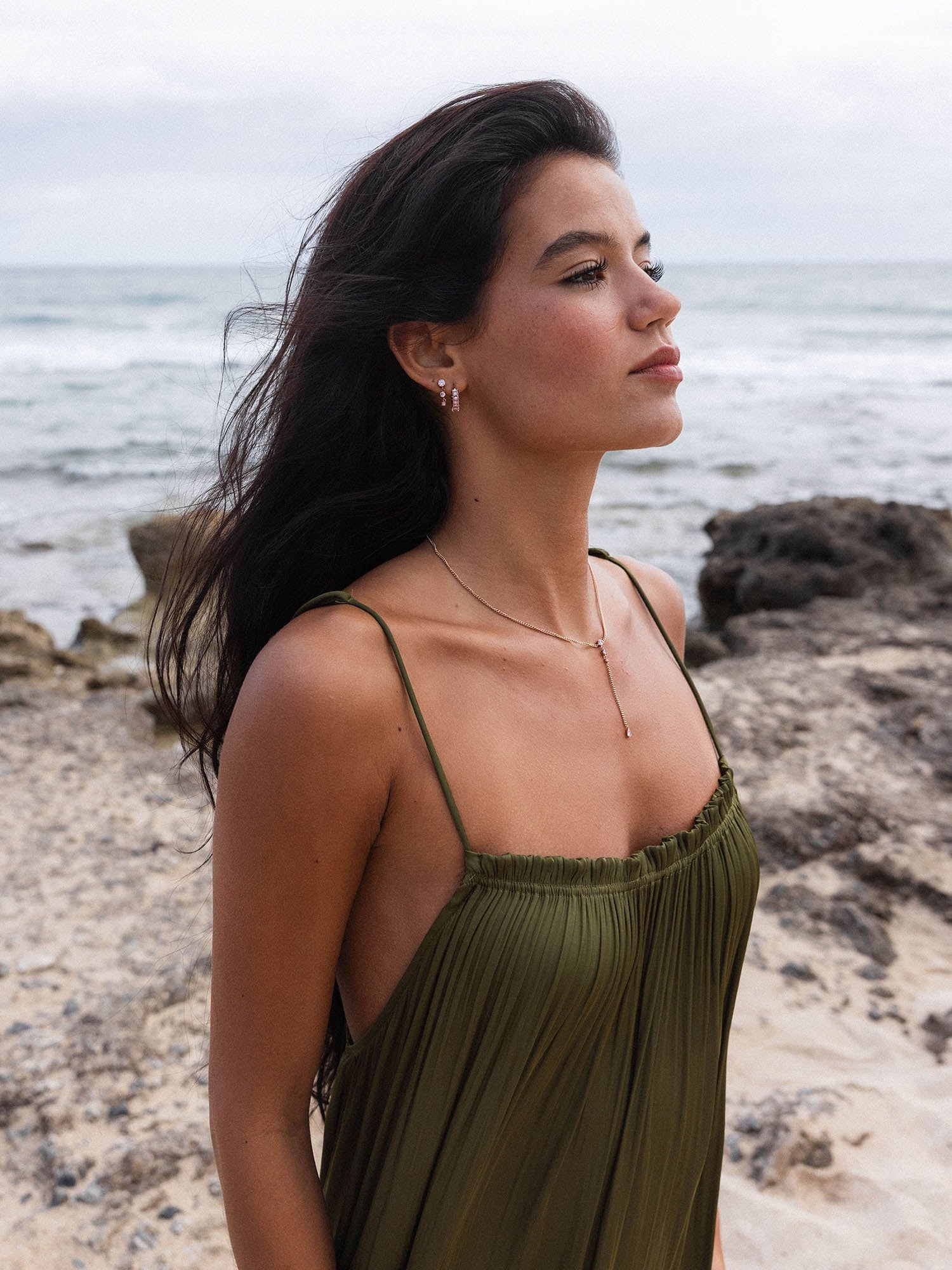 Elegante, silberne Ohrringe und zarte Kette von PURELEI, getragen am Strand mit sanften Wellen im Hintergrund.
