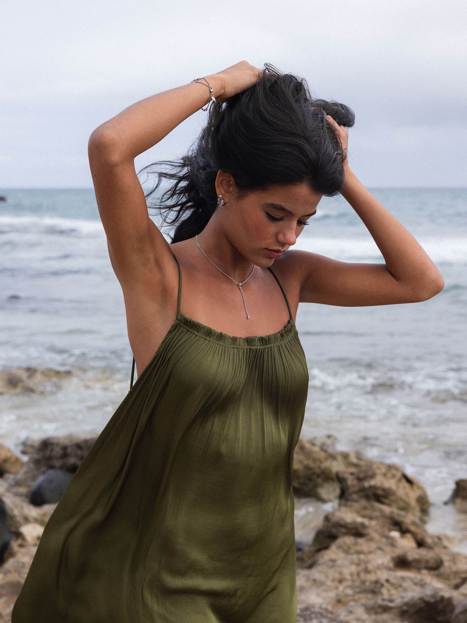 Elegante, grüne PURELEI Kette, getragen am Strand mit sanften Wellen im Hintergrund.
