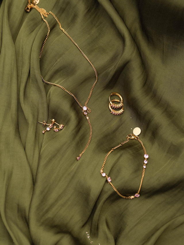 Zarte goldene Schmuckstücke von PURELEI auf weichem, olivgrünem Stoff drapiert.