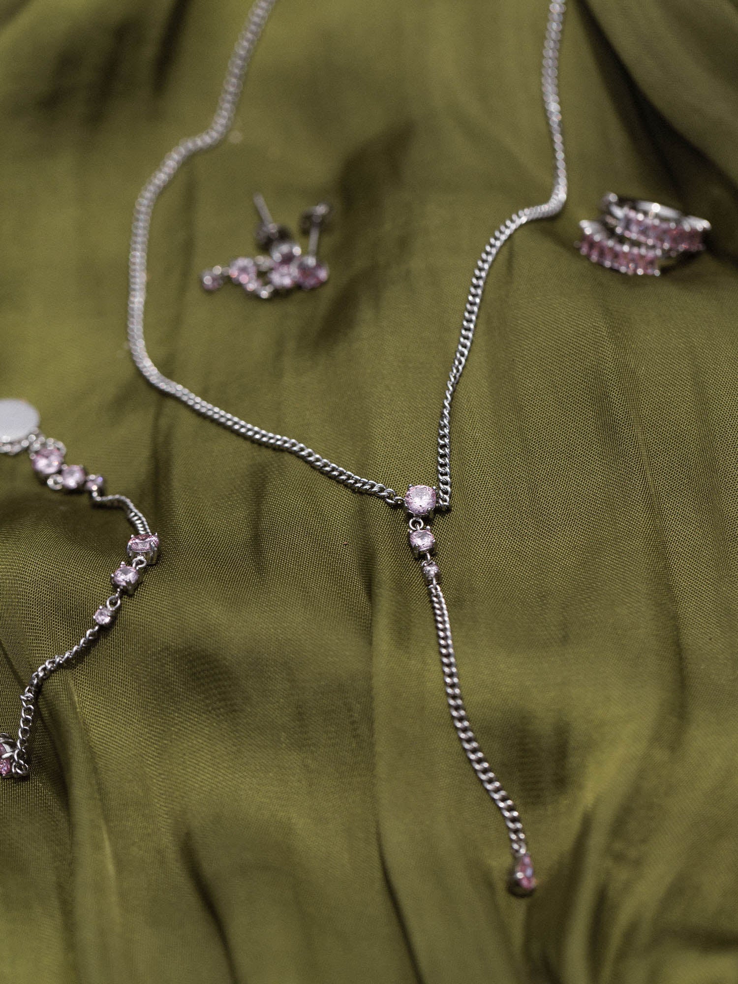 Silberne Kette mit funkelnden Details auf grünem Stoff, PURELEI inspiriert.