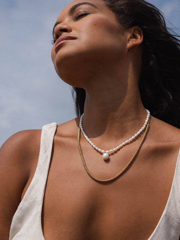 Zarte PURELEI Kette mit Muschelanhänger und goldener Kette, strahlend im Sonnenlicht.