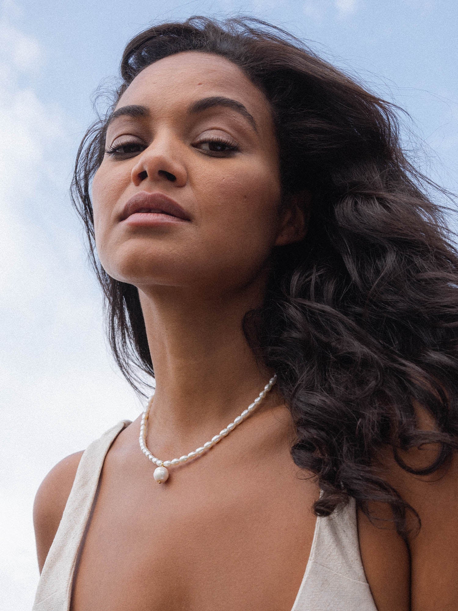 Perlenkette von PURELEI, elegant und feminin, vor blauem Himmel getragen.