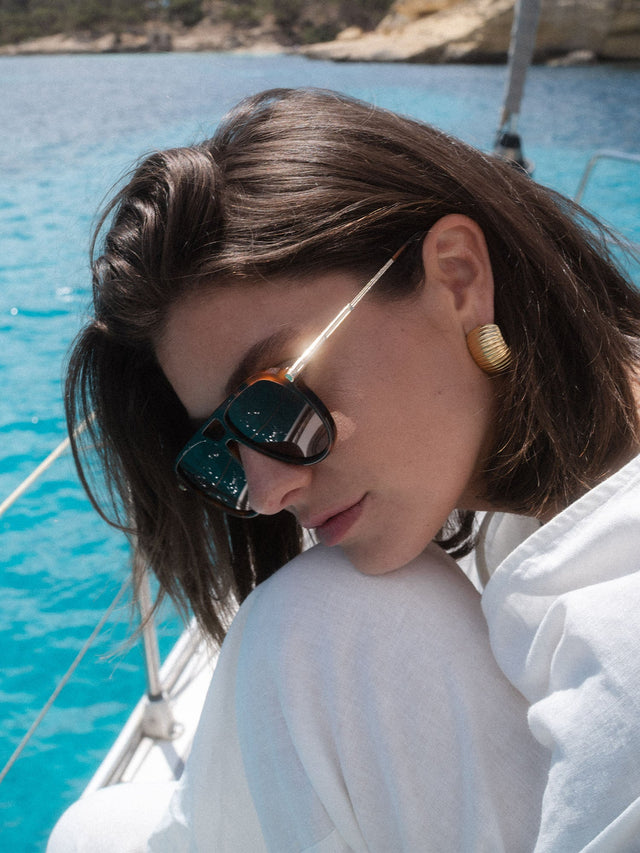 PURELEI Palm Beach Sonnenbrille im braunen Schildpatt-Look mit goldenem Bügel, elegant am Sommerstrand getragen.