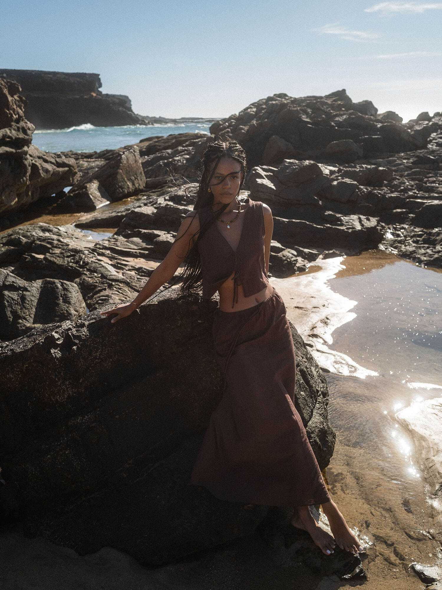Braunes, luftiges Outfit am Strand, umgeben von Felsen, inspiriert von PURELEI.