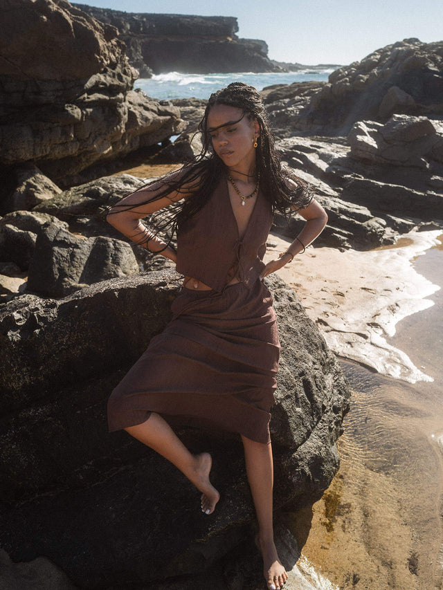 Braunes, luftiges Outfit am Strand, umgeben von Felsen, inspiriert von PURELEI.