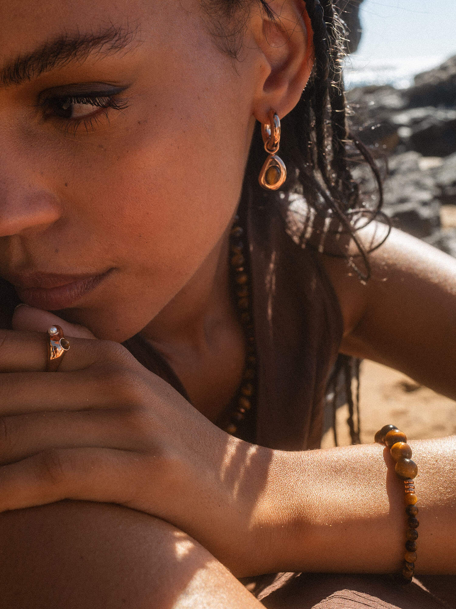 Goldene Ohrringe und Ring von PURELEI, getragen am Strand, strahlen tropische Eleganz aus.
